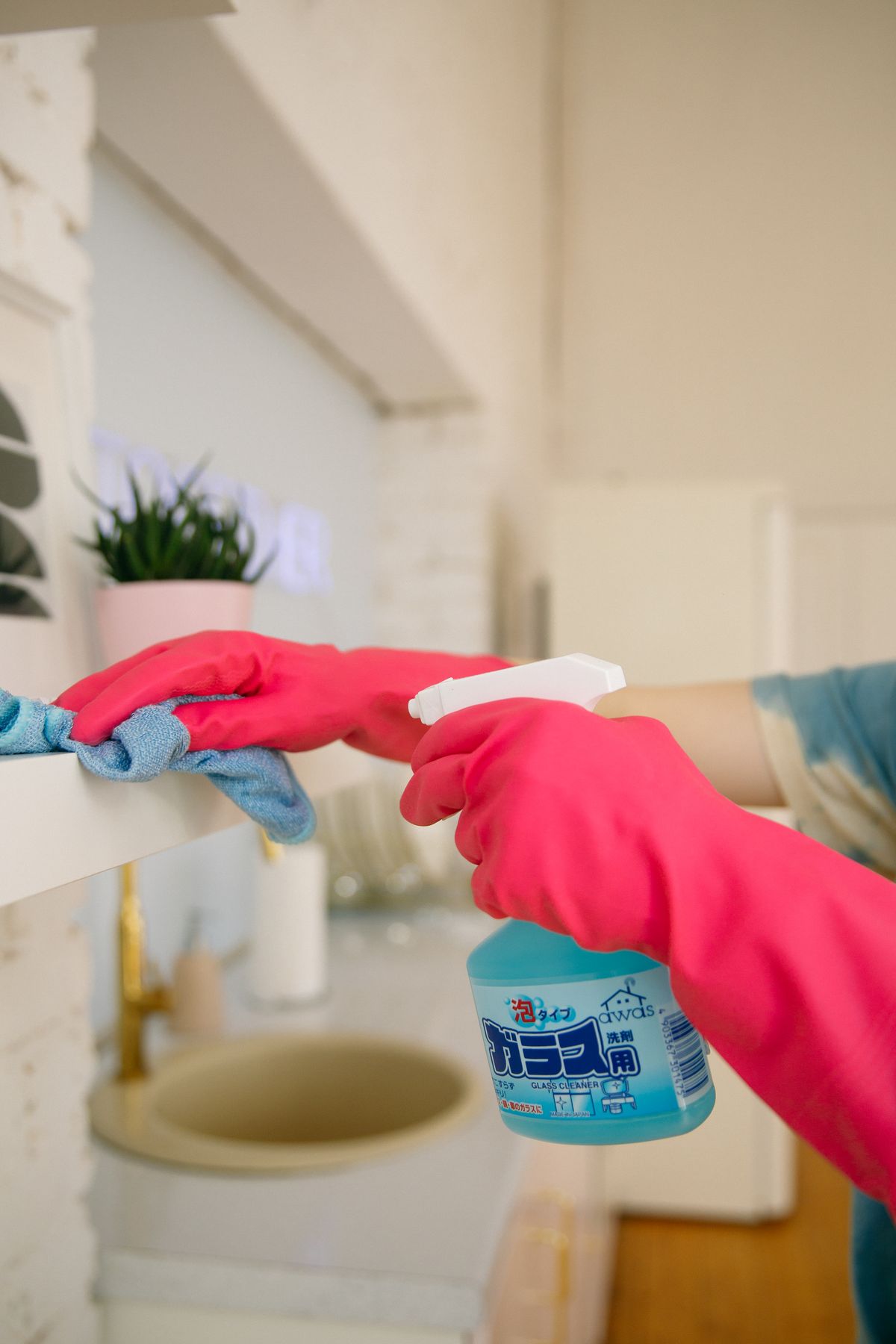Gloved hands wiping a shelf with a cloth and spray cleaner